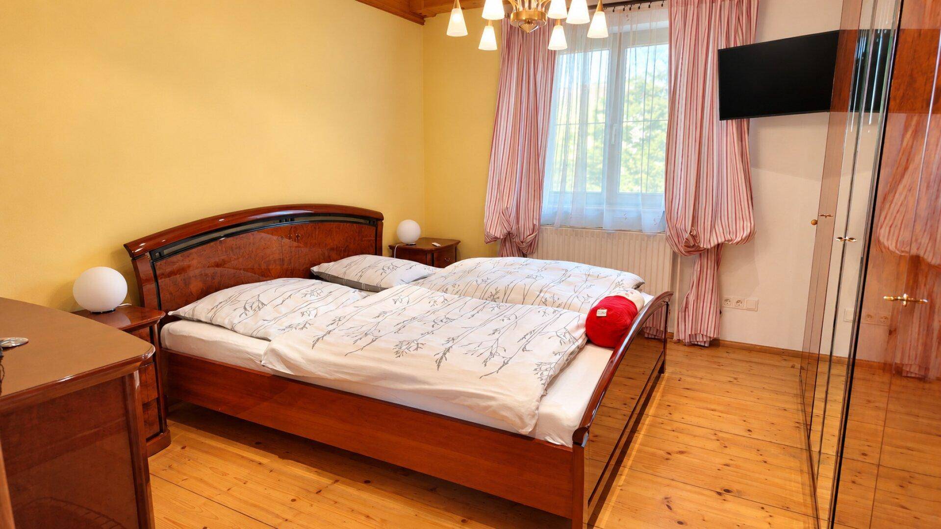 Gemütliches Schlafzimmer mit Holzboden, Doppelbett und einem Fenster mit gestreiften Vorhängen.