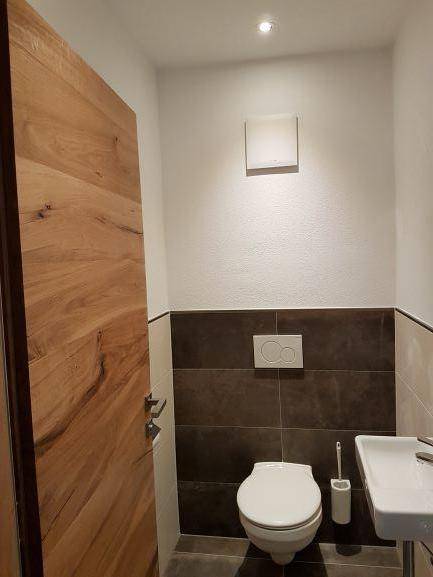 Modernes Gäste-WC mit dunklen und hellen Fliesen sowie einer Holztür.
