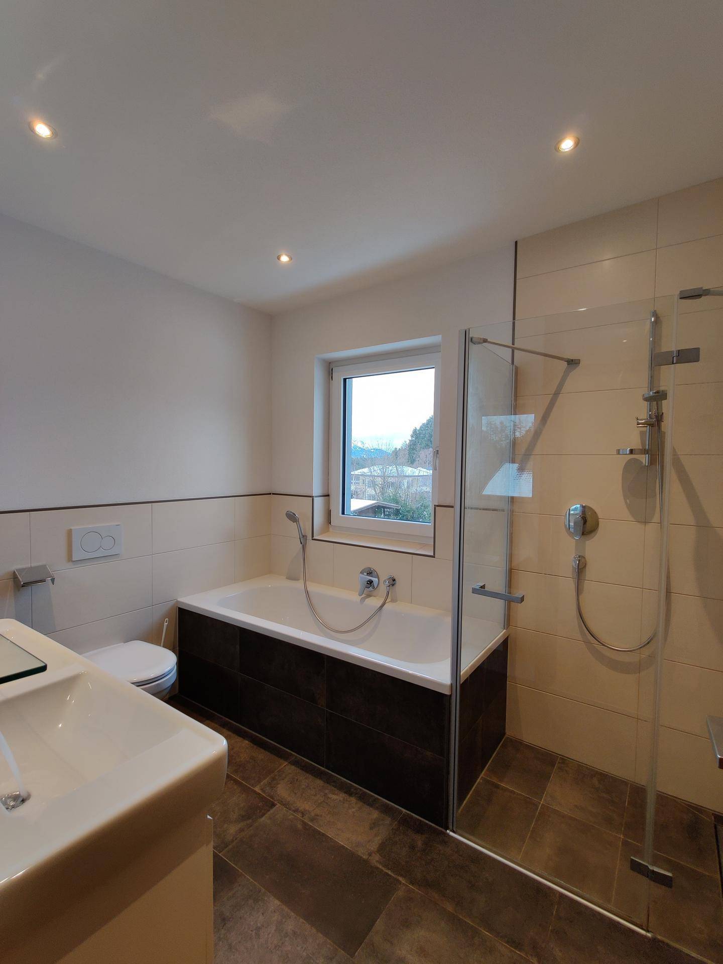 Helles Badezimmer mit Badewanne, Dusche und Fenster mit Bergblick.