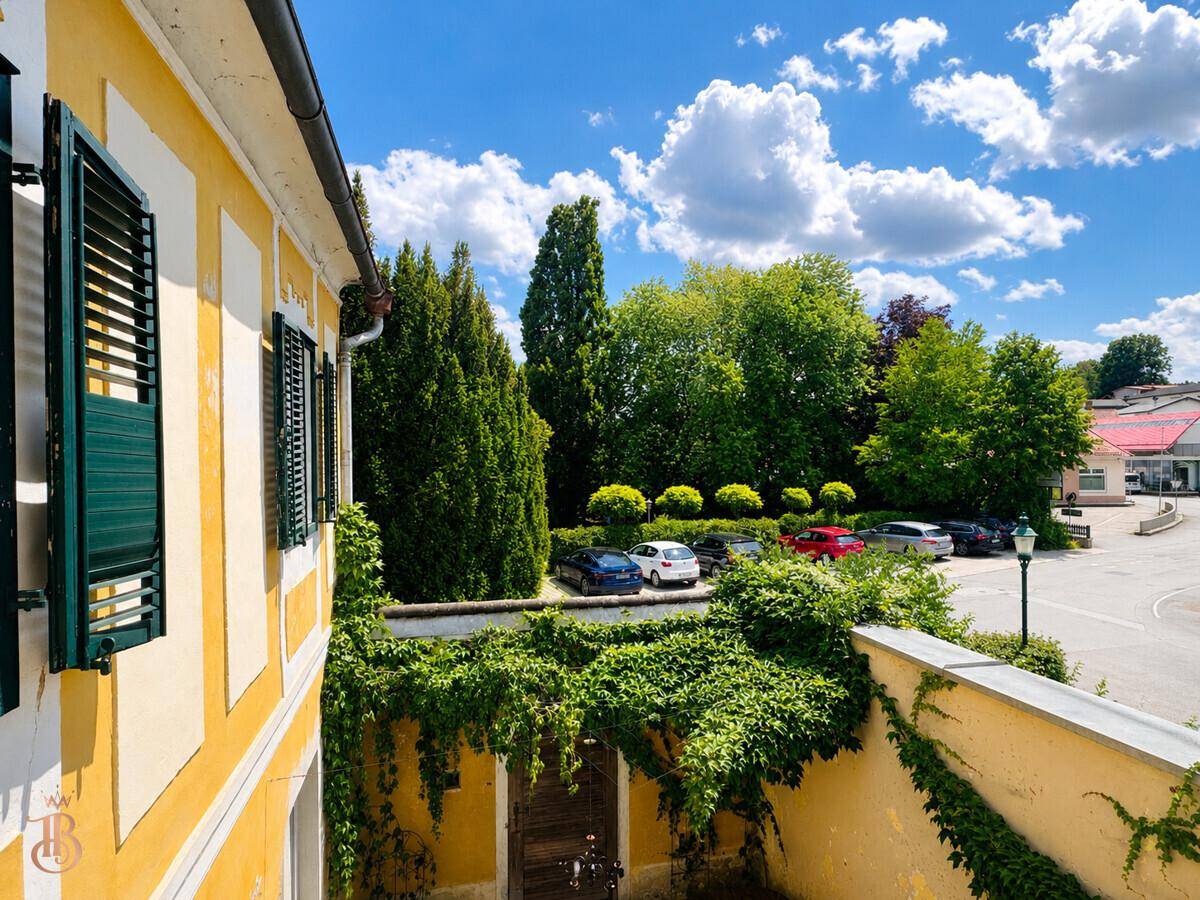 Blick vom Balkon auf den Parkplatz und die grüne Umgebung unter blauem Himmel.