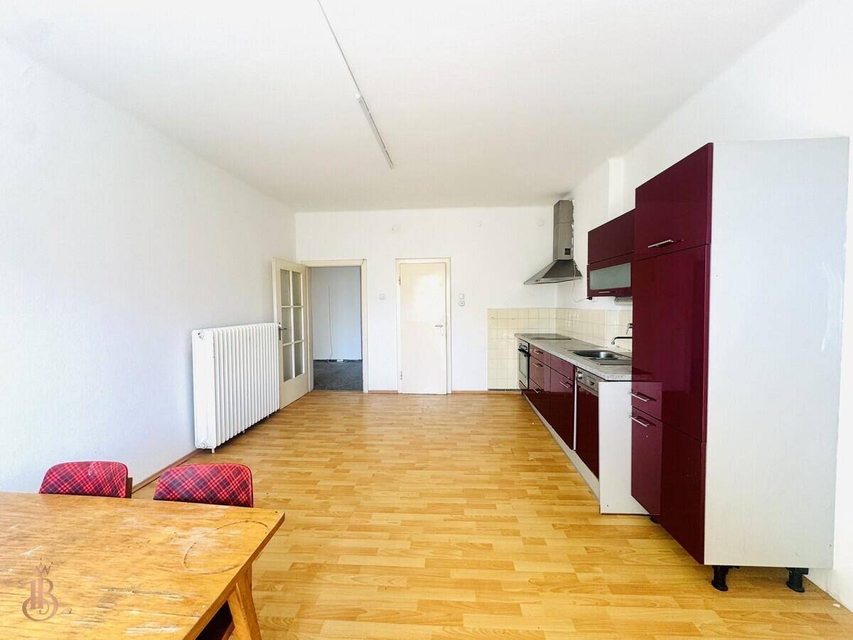 Geräumiger Wohn-Essbereich mit Küchenzeile, Laminatboden und Zugang zu weiteren Räumen.