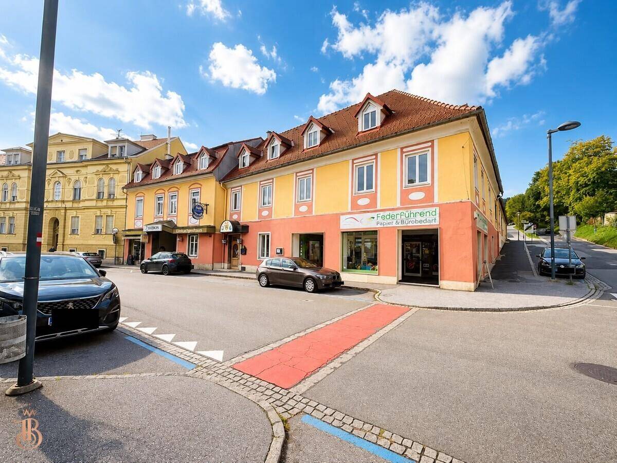 Gebäudeansicht mit geparkten Autos auf der Straße und klarem Himmel.
