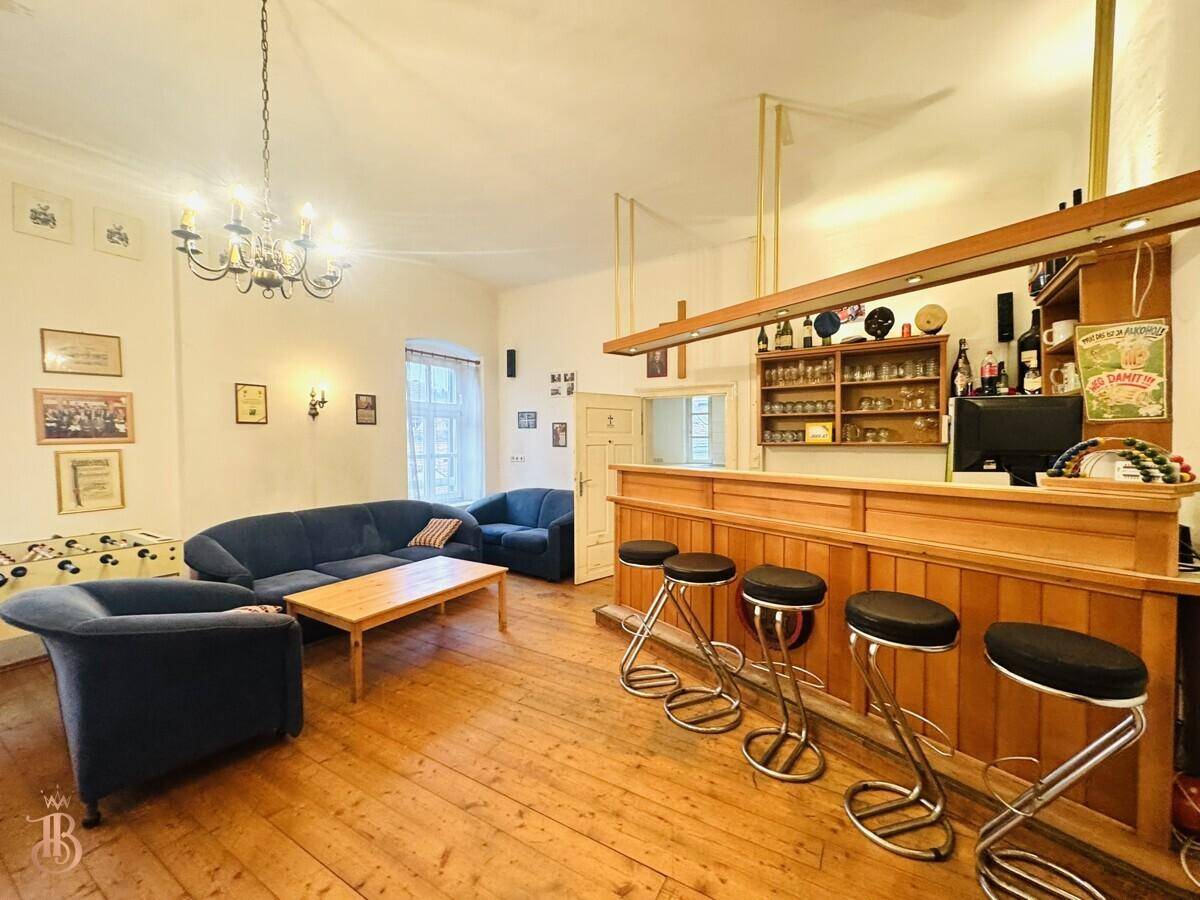 Barbereich im Gemeinschaftsraum mit Sitzgelegenheiten, Holzboden und hohen Decken, ideal für Unterhaltung.