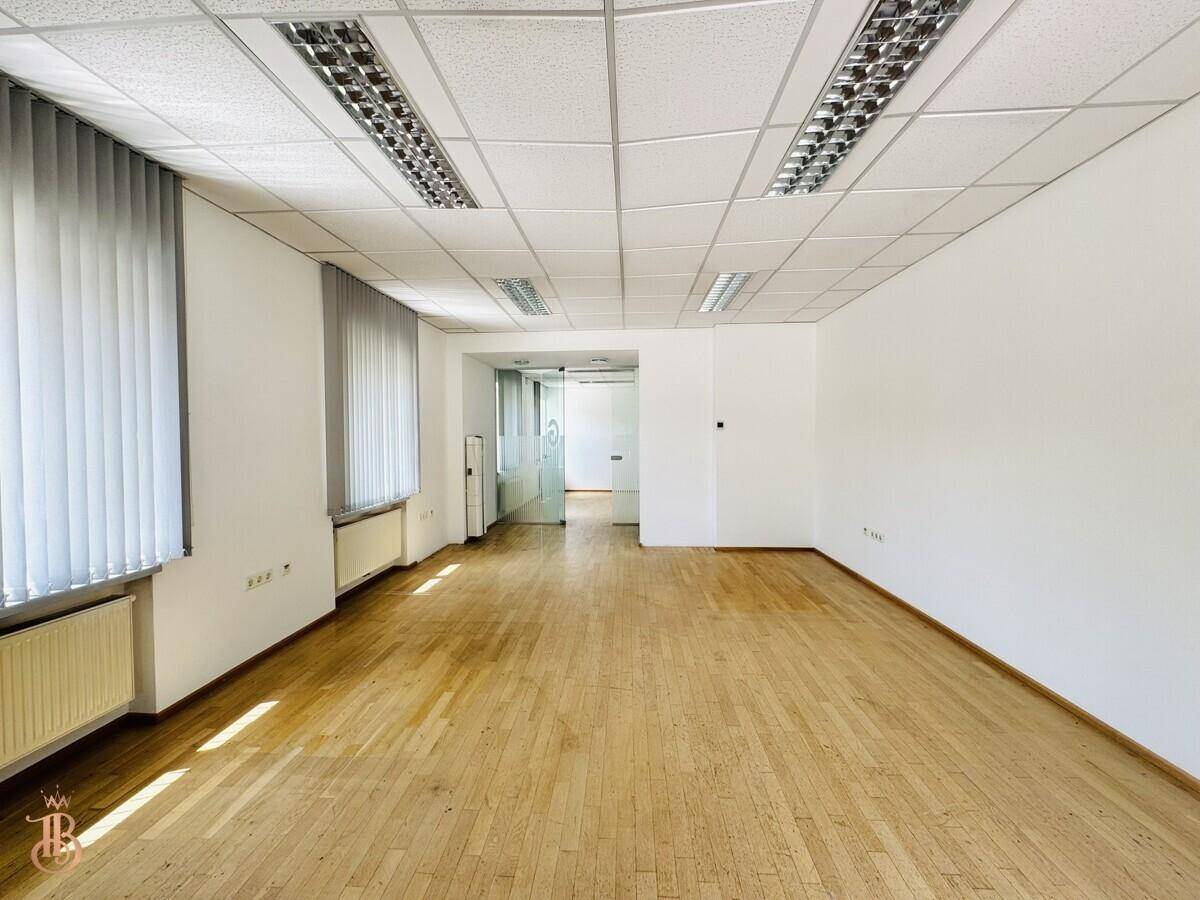 Weitläufiger Bürobereich mit Laminatboden und Fenstern, die viel Tageslicht hereinlassen.