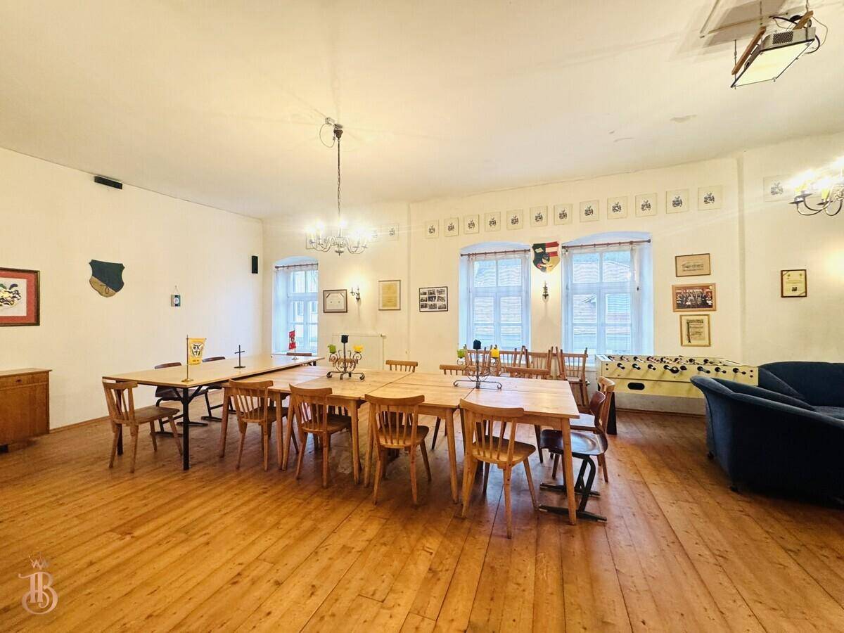 Großer Gemeinschaftsraum mit mehreren Esstischen, Holzboden und hohen Decken, ideal für Veranstaltungen.