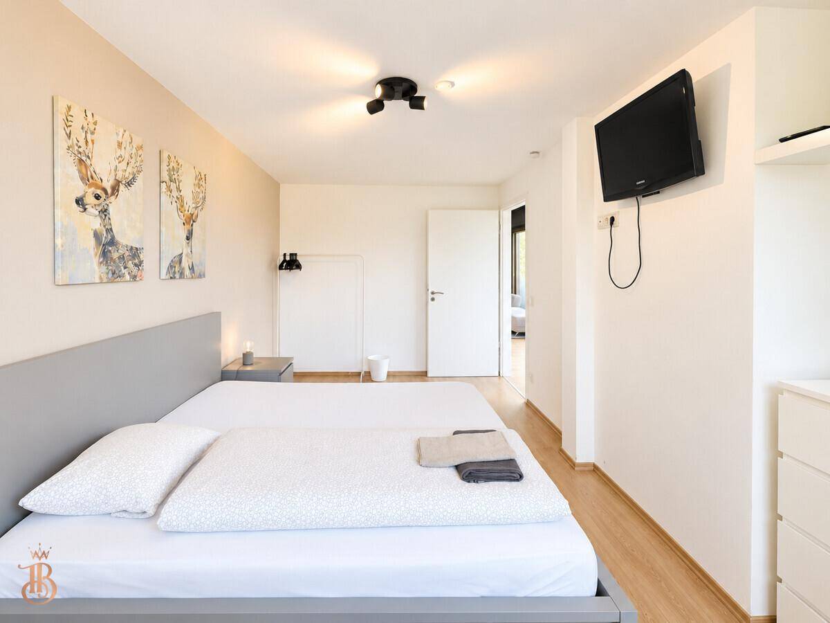 Schlafzimmer mit Doppelbett, Wandfernseher und schlichter, moderner Einrichtung.