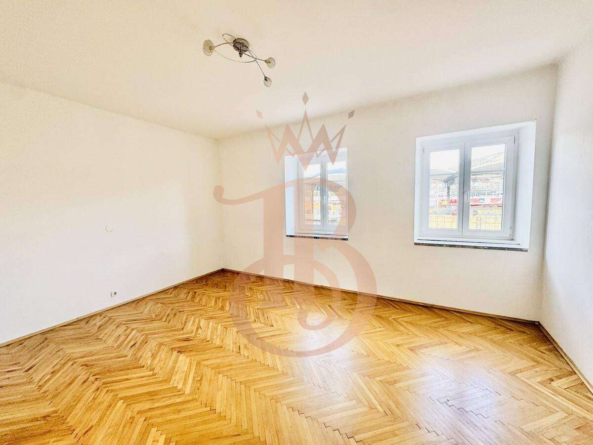 Geräumiges Zimmer mit Fischgrätparkett und zwei großen Fenstern für optimale Belichtung.