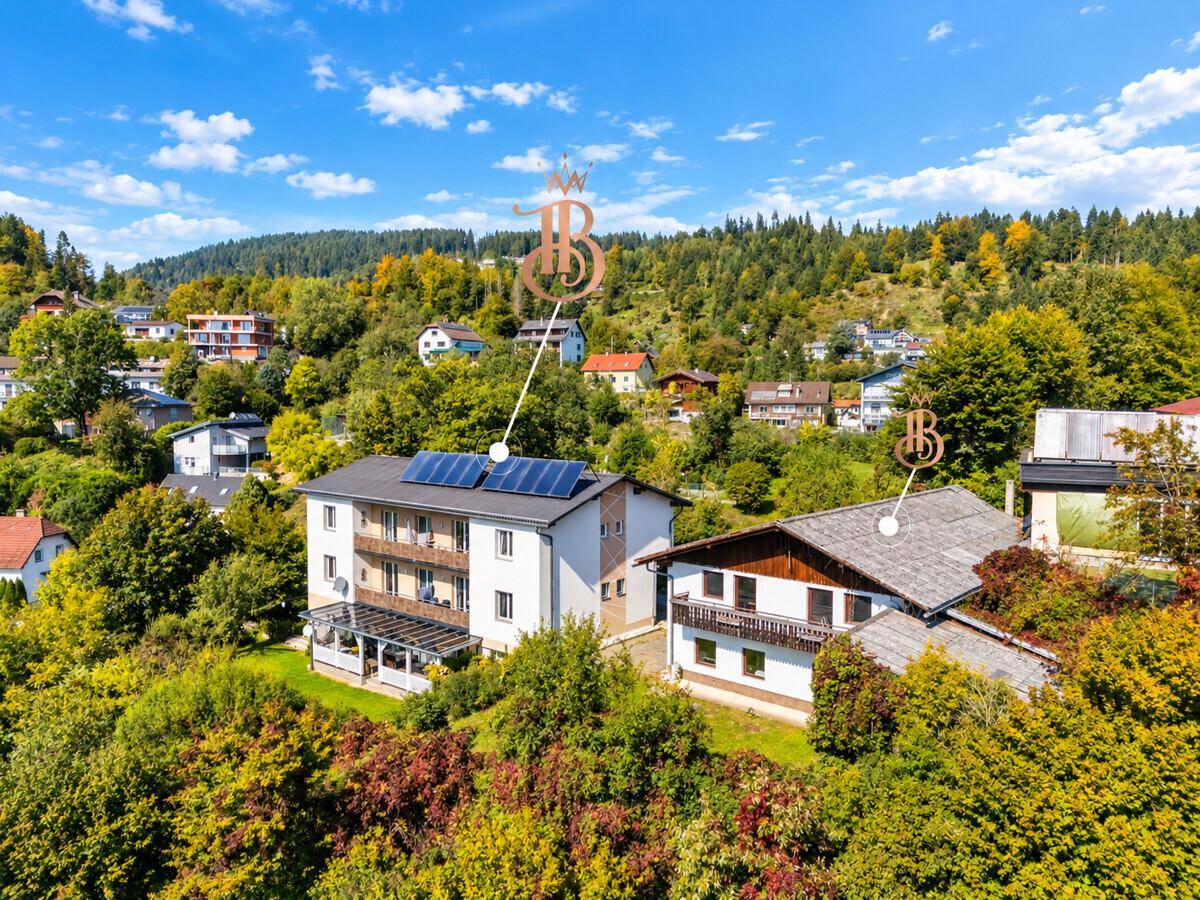Überblick über das Anwesen mit Hauptgebäude und Nebengebäude, eingebettet in eine bewaldete Hügellandschaft.