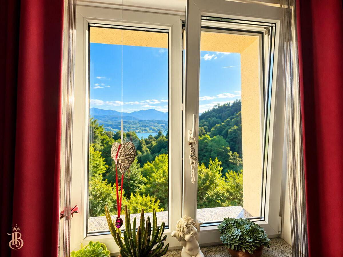 Fensterblick auf die malerische Seen- und Berglandschaft, umrahmt von roten Vorhängen.