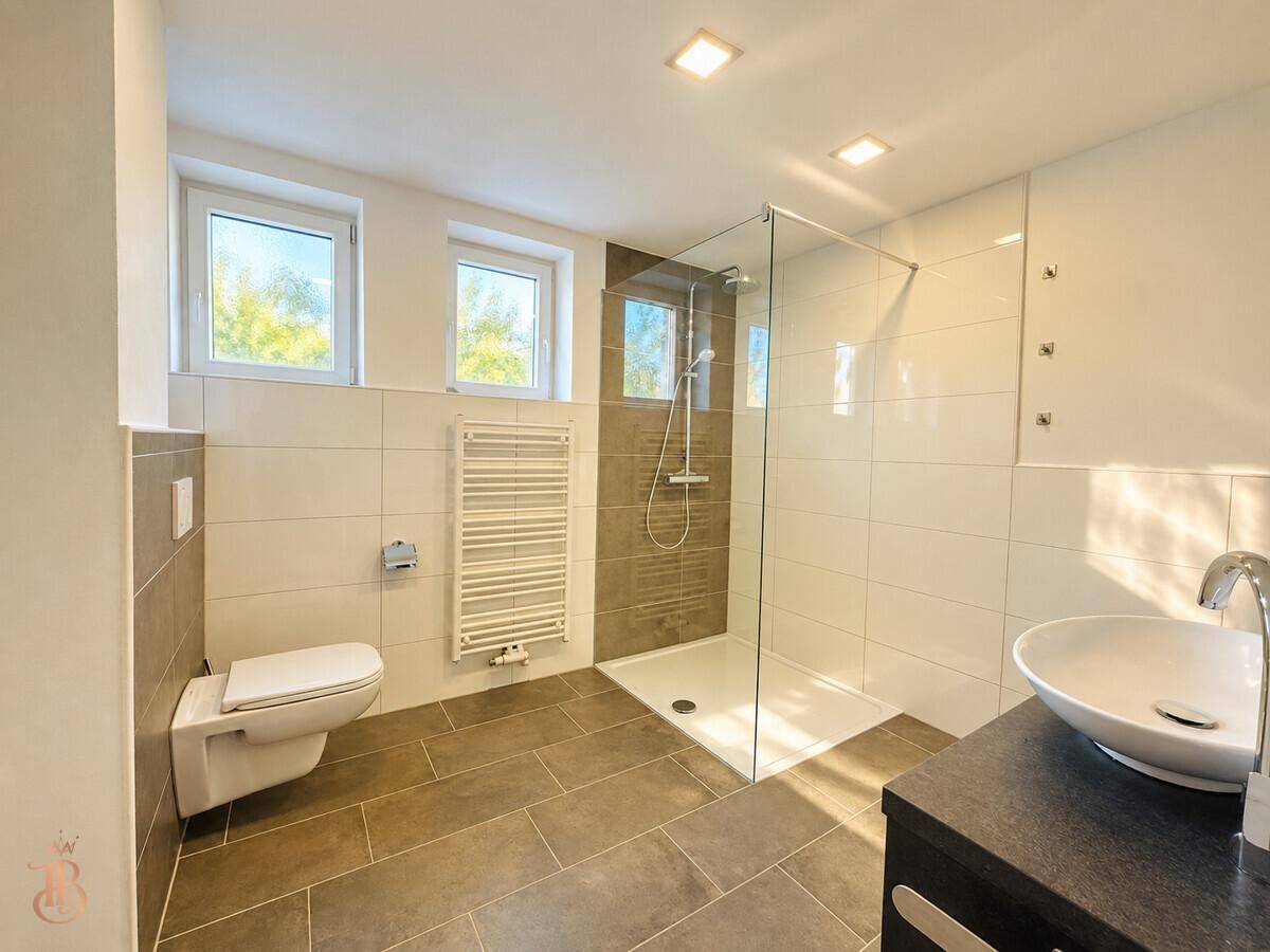 Helles Badezimmer mit moderner Dusche, wandhängendem WC und Fenster für Tageslicht.