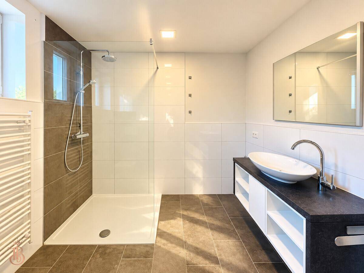 Modernes Badezimmer mit ebenerdiger Dusche, großem Waschtisch und beheiztem Handtuchhalter.
