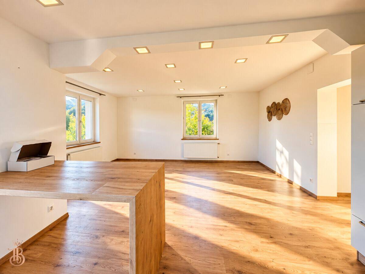 Heller Wohnbereich mit Holzboden und großen Fenstern, die viel Tageslicht hereinlassen.