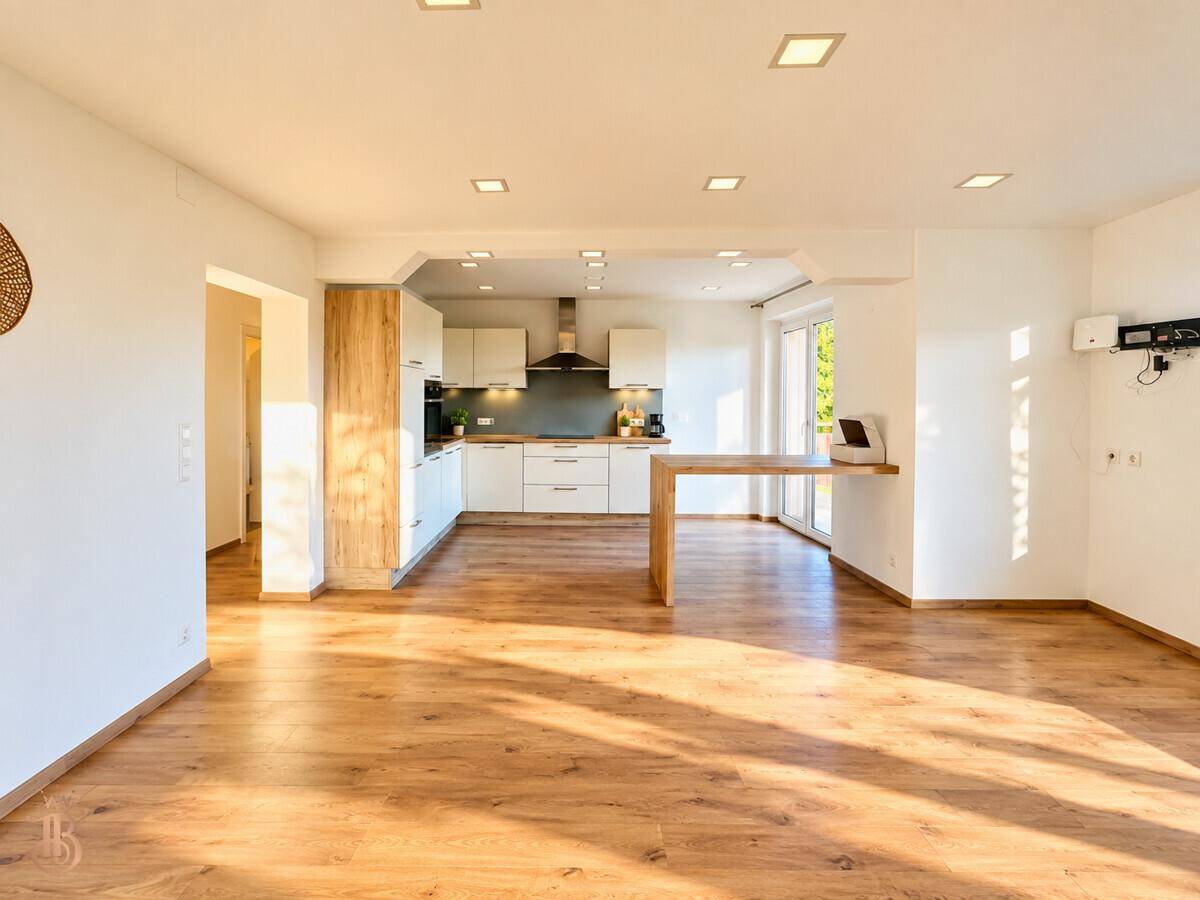 Offener Wohnbereich mit integrierter moderner Küche und Holzboden, lichtdurchflutet.