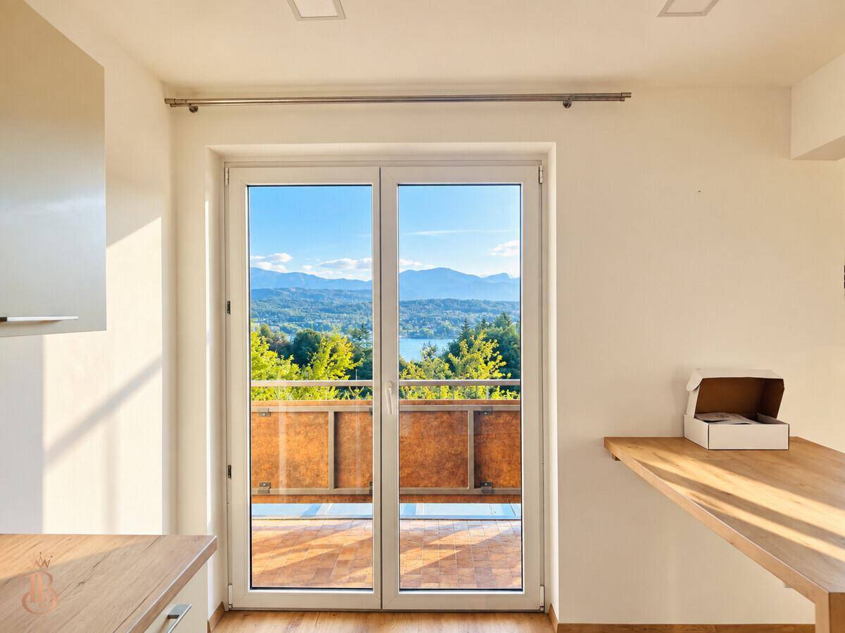 Heller Innenraum mit Balkonzugang und weitem Blick auf den See und die Berge.