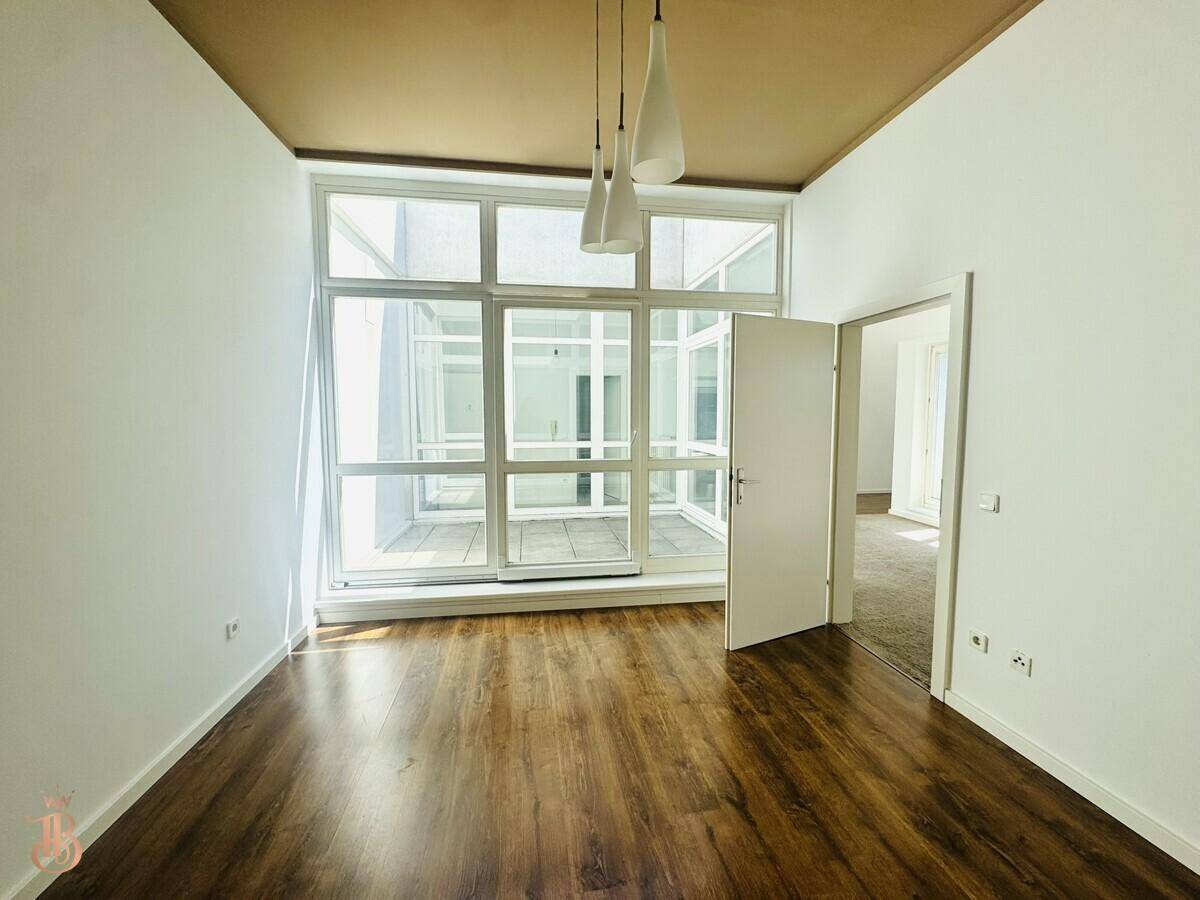 Heller Raum mit Holzboden, brauner Decke und großen Fenstern, die viel Licht hereinlassen.