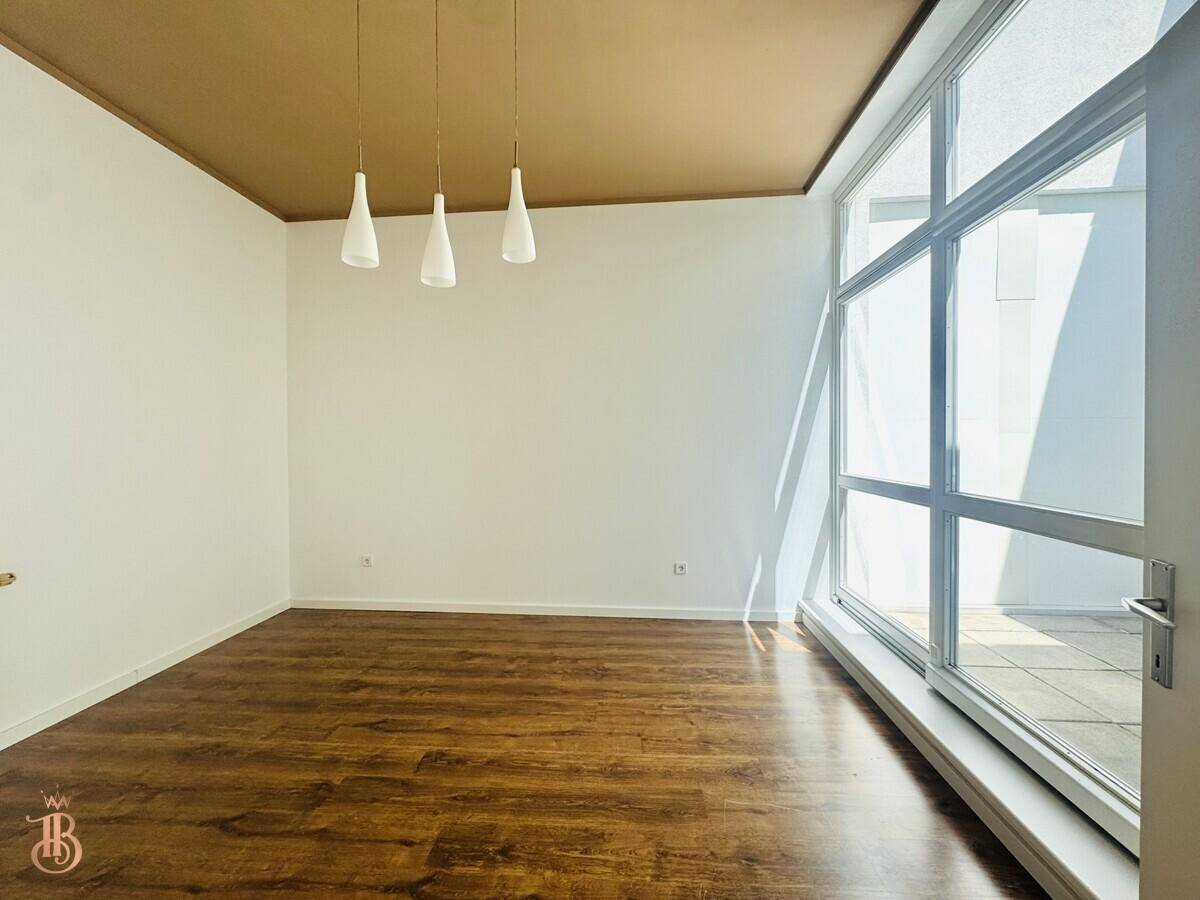 Leerer Raum mit Holzboden, brauner Decke und großen Fensterfronten mit Zugang nach draußen.