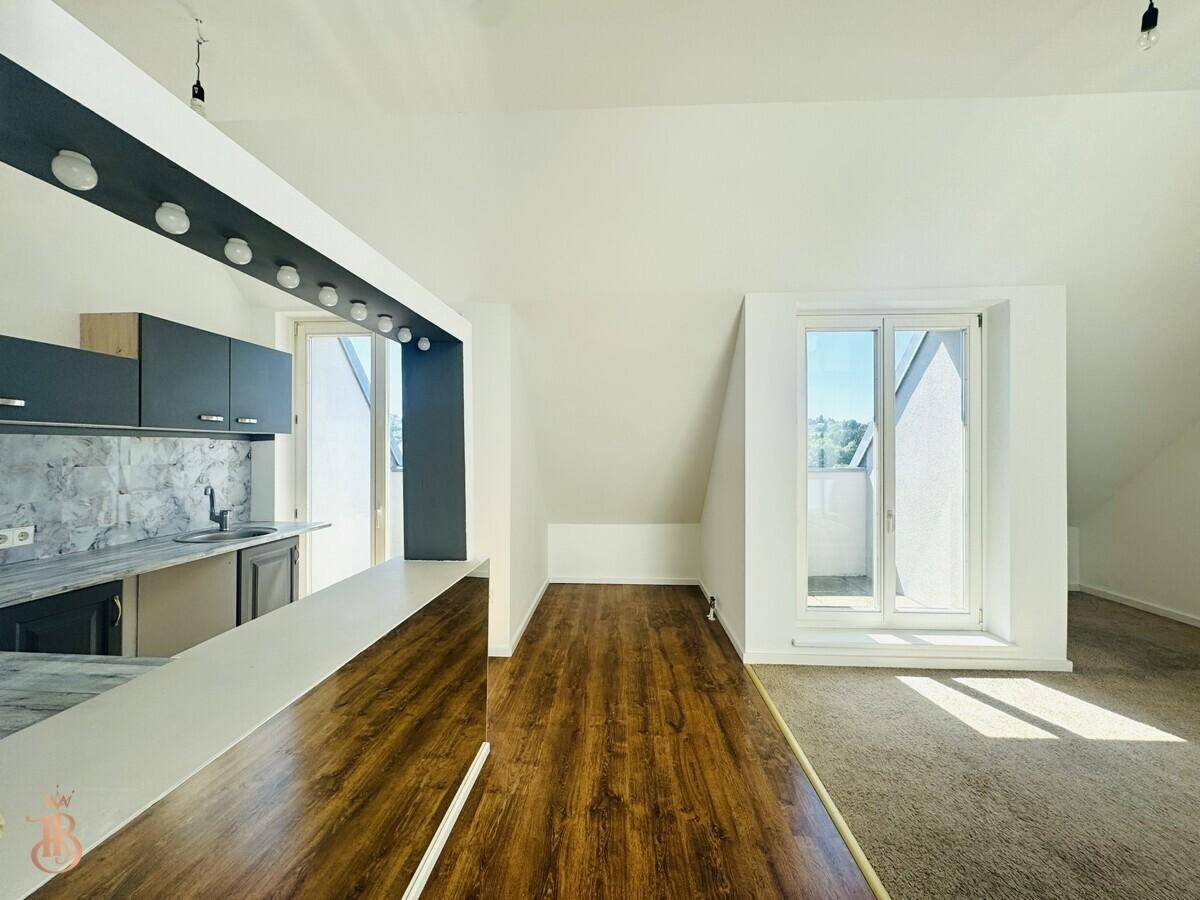 Offener Wohnbereich mit Küchenzeile, Teppichboden und Zugang zu einem Balkon oder einer Terrasse.