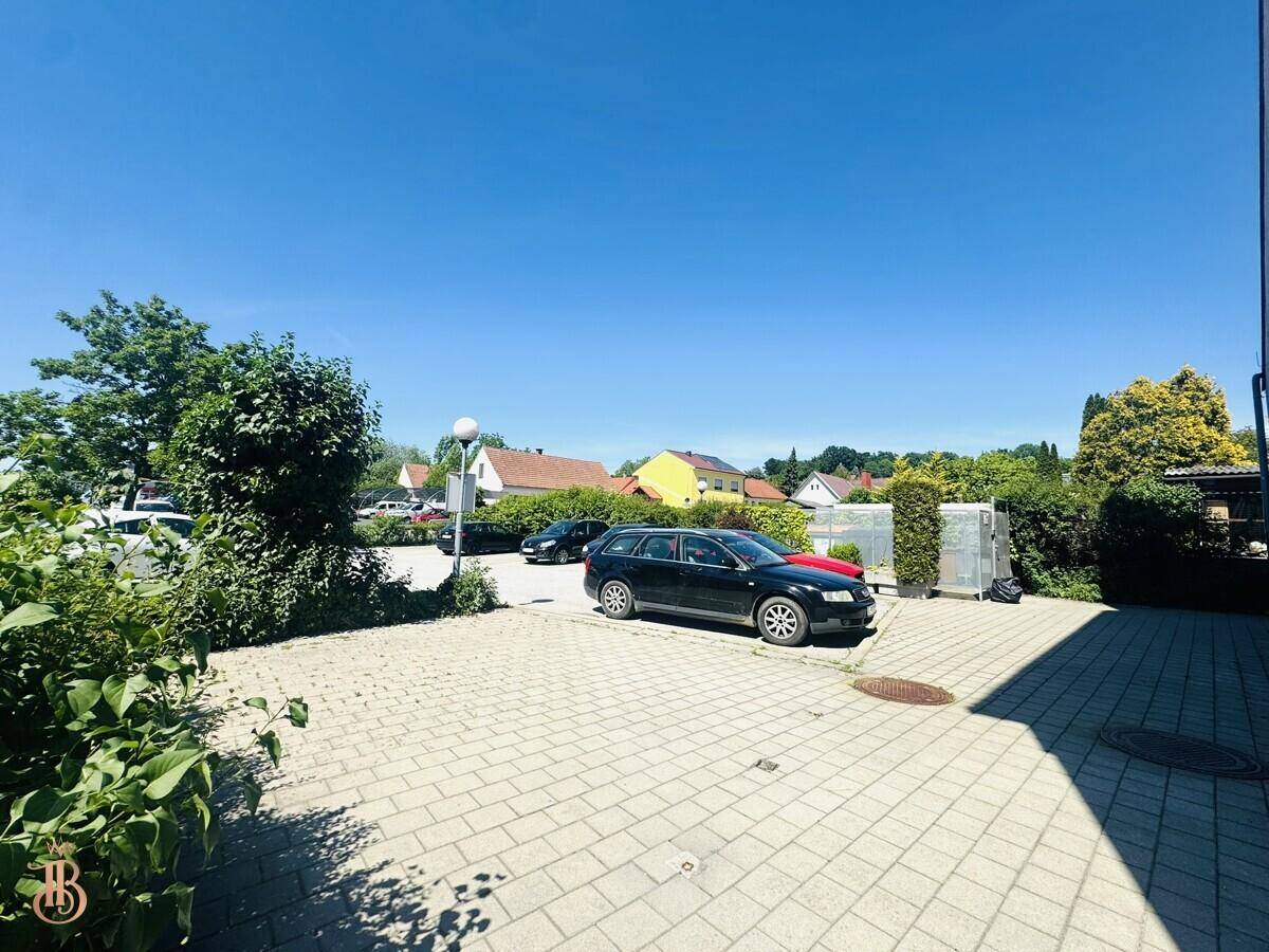Außenparkplatz mit gepflastertem Bereich und umliegender Wohnbebauung unter blauem Himmel.