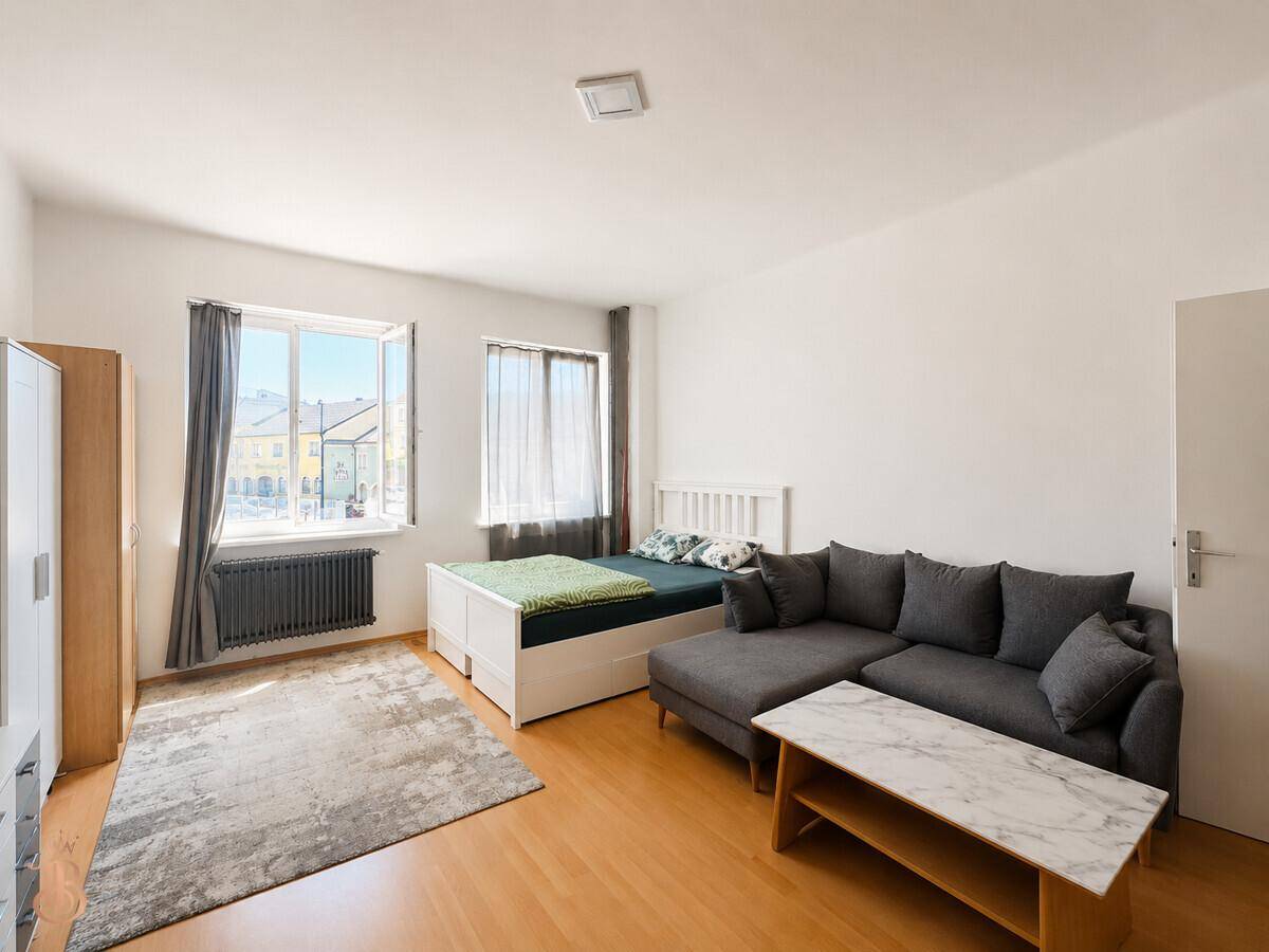 Heller Wohn- und Schlafbereich mit großem Fenster, Sofa und Bett.