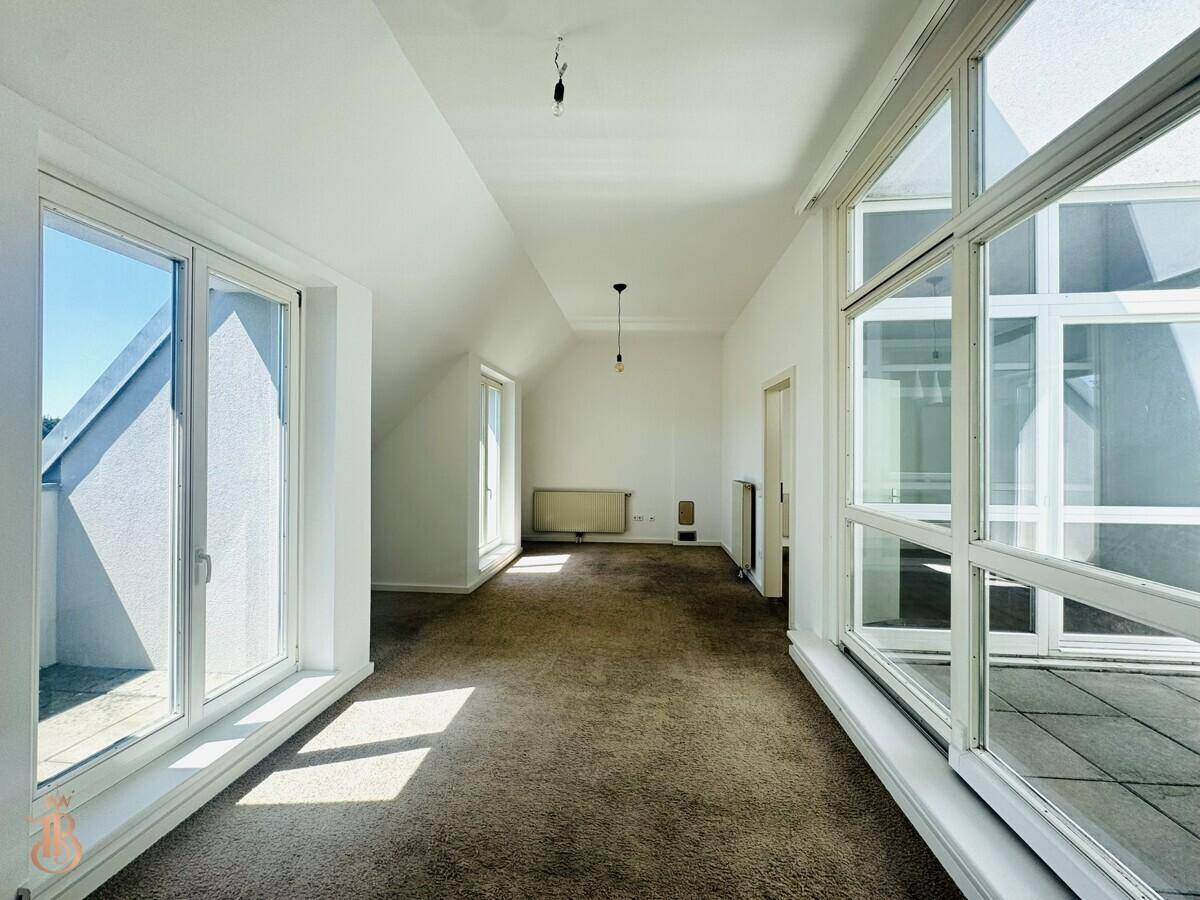 Heller, leerer Raum mit Teppichboden, Dachschräge und großen Fenstern zur Terrasse.