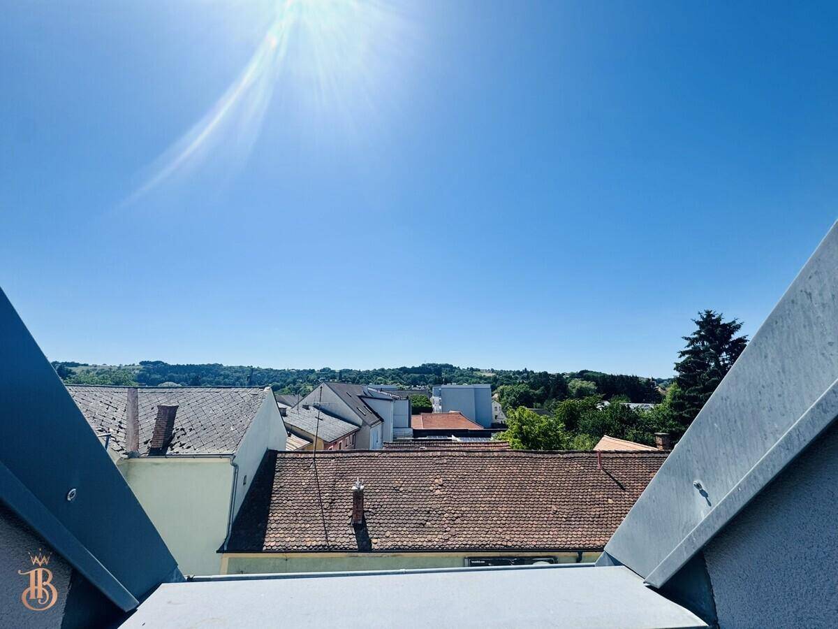 Weitblick über Dächer und grüne Hügel unter strahlend blauem Himmel.
