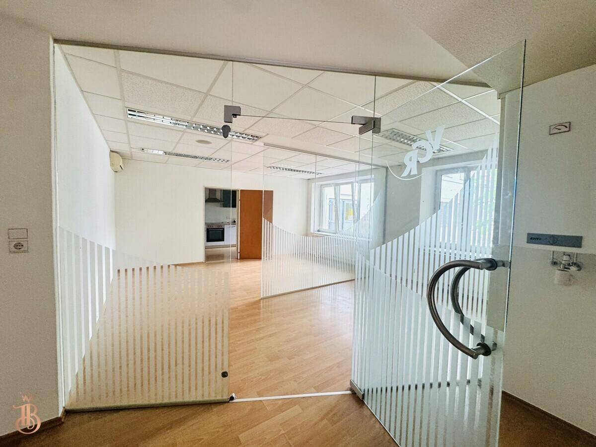 Blick durch die Glastüren in einen Büroraum mit Holzfußboden und angrenzender Küche.