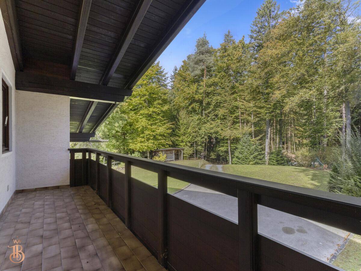 Überdachter Balkon mit Fliesenboden und Blick ins Grüne sowie auf den Wald.