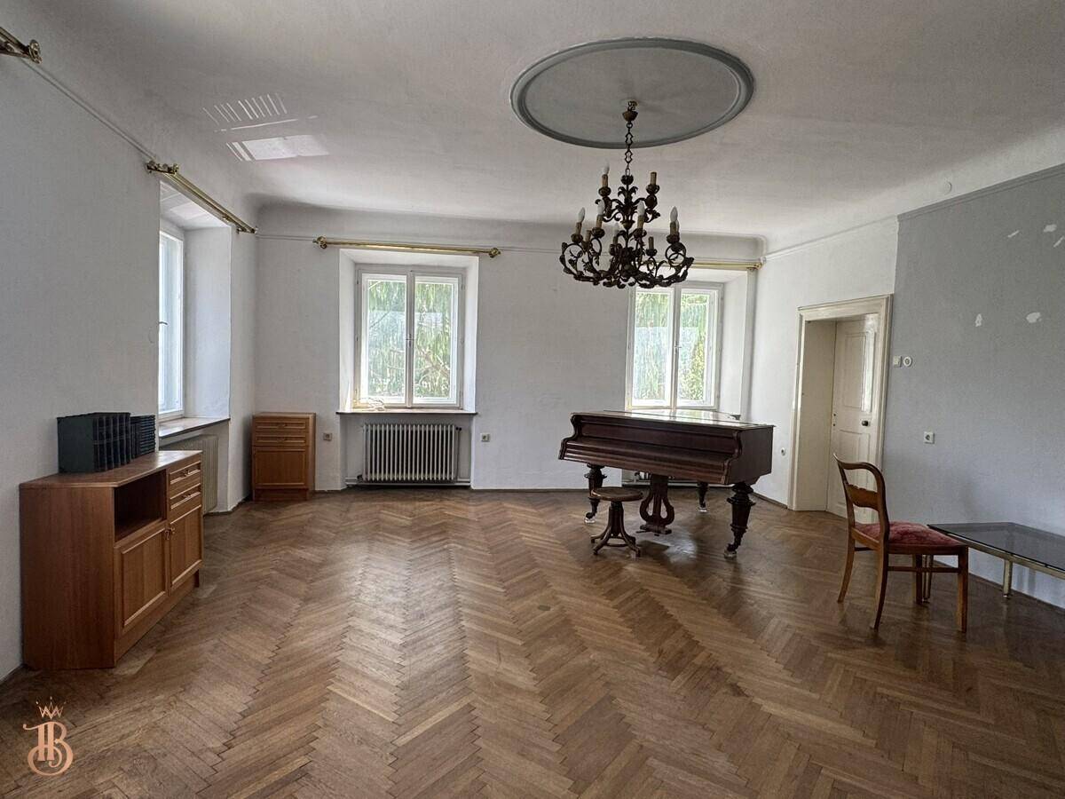 Eleganter Wohnraum mit Fischgrätparkett, Kronleuchter und einem Flügel als zentrales Element.