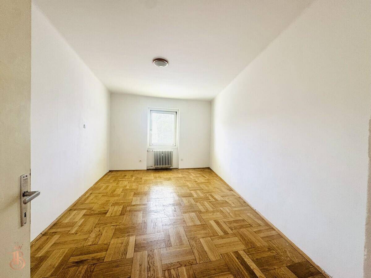 Schlichtes Zimmer mit Fischgrätparkett, weiß gestrichenen Wänden und einem einzelnen Fenster.