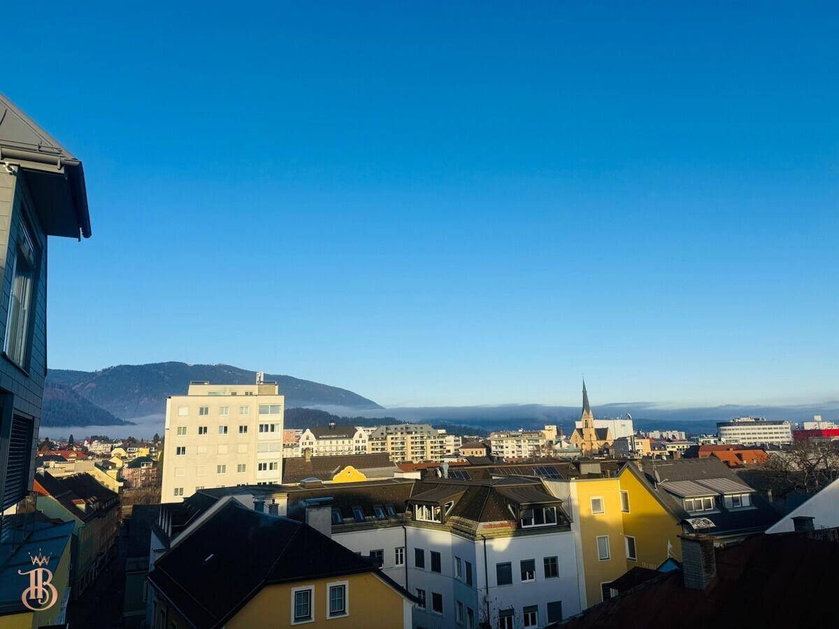 Weitblick über die Dächer der Stadt mit majestätischen Bergen am Horizont unter klarem Himmel.