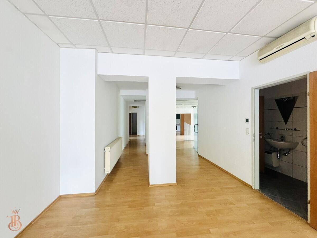 Langer Flur mit Laminatboden und Zugang zu einem Raum mit Waschbecken, ideal für Büroflächen.