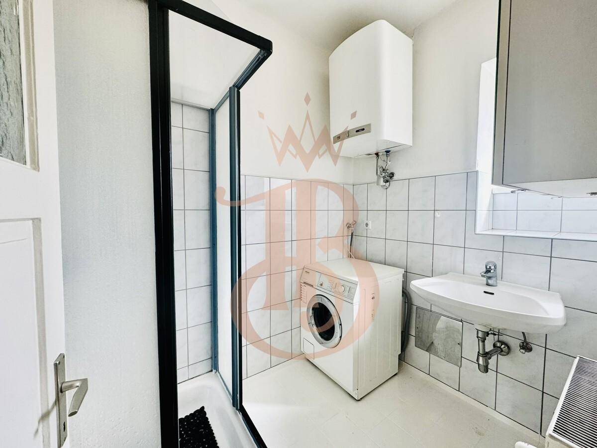 Badezimmer mit Duschkabine, Waschbecken und Waschmaschine, hell gefliest und praktisch.