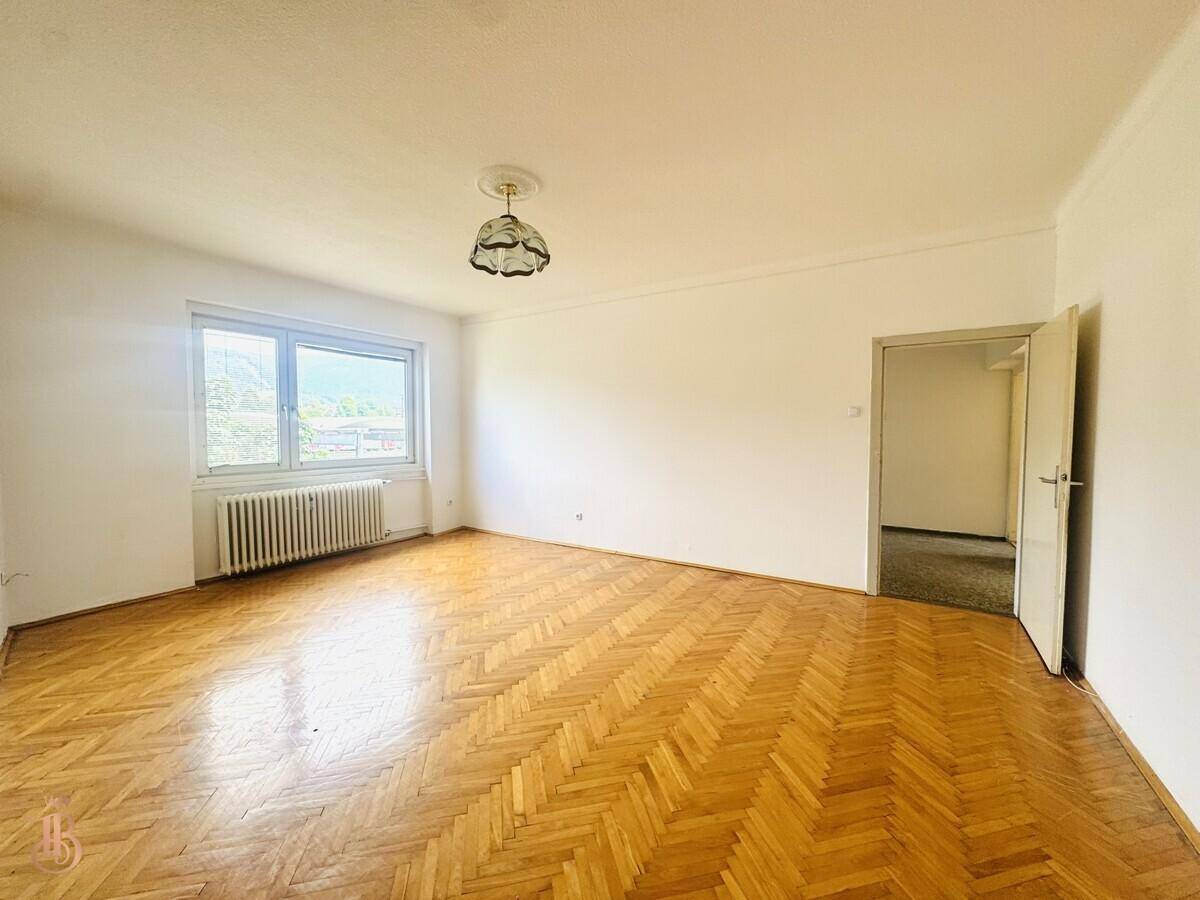 Geräumiges Zimmer mit Fischgrätparkett, weiß gestrichenen Wänden und Zugang zu einem weiteren Raum.