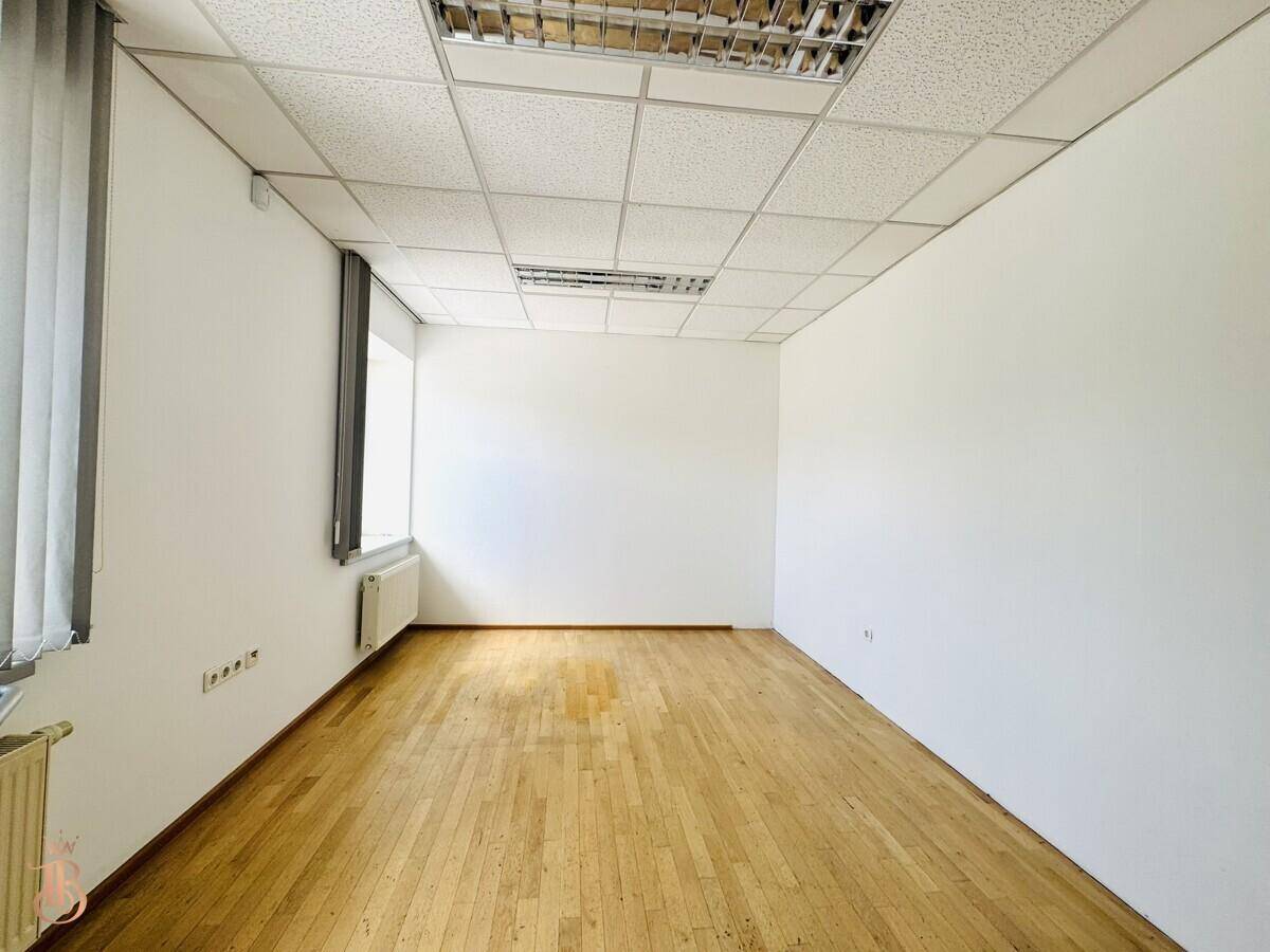 Leerer Büroraum mit Holzfußboden, weißen Wänden und einem Fenster mit Jalousien.