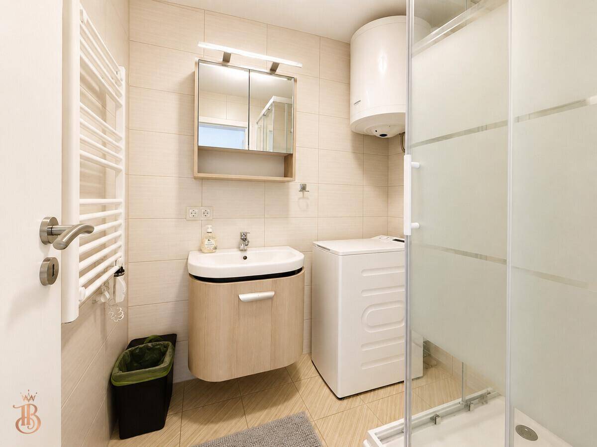 Modernes Badezimmer mit Dusche, Waschbecken, Spiegelschrank und integrierter Waschmaschine.