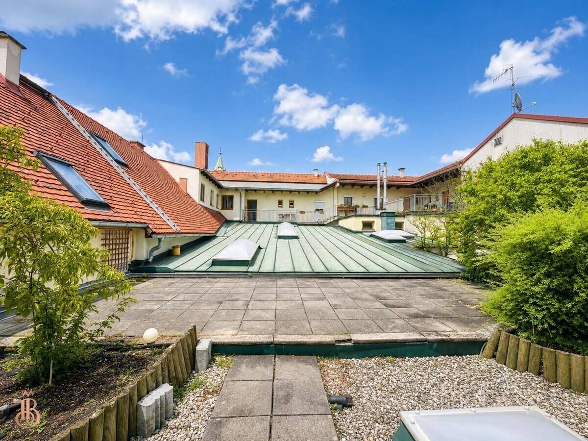 Geräumige Dachterrasse mit Steinplatten, Kies und grünen Pflanzen, umgeben von Gebäuden.