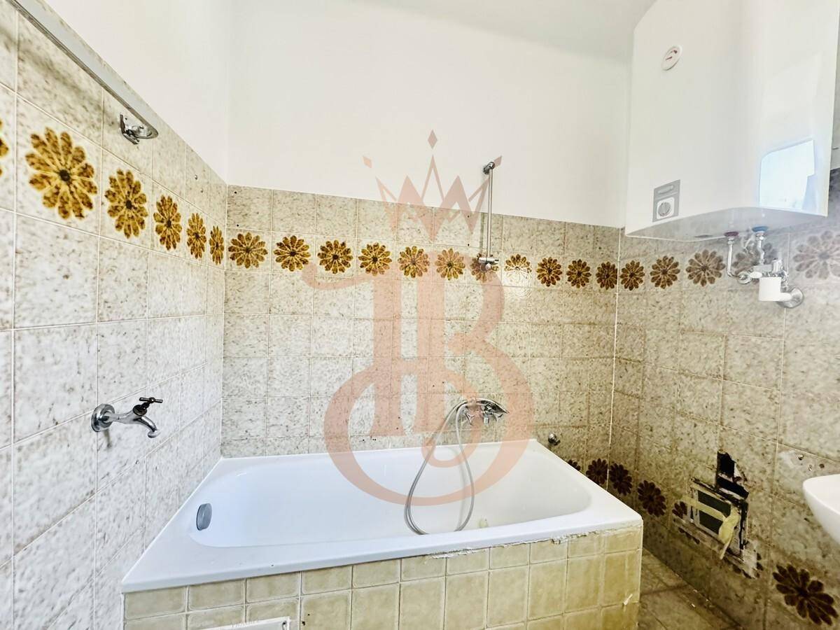 Badezimmer mit Badewanne, Waschbecken und Waschmaschine, umgeben von gemusterten Fliesen im 80er-Jahre-Stil.