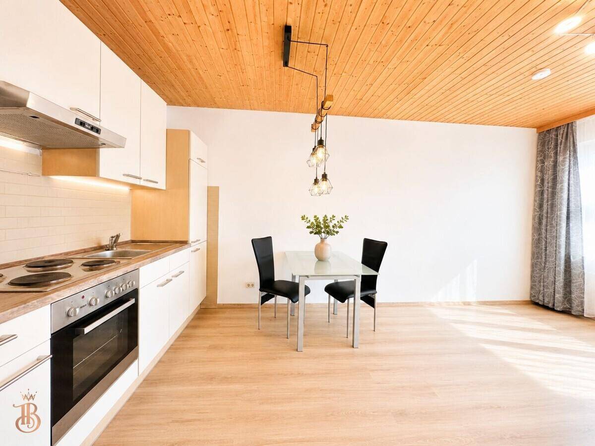 Moderne Küchenzeile mit weißen Schränken, integriertem Backofen und Essbereich.