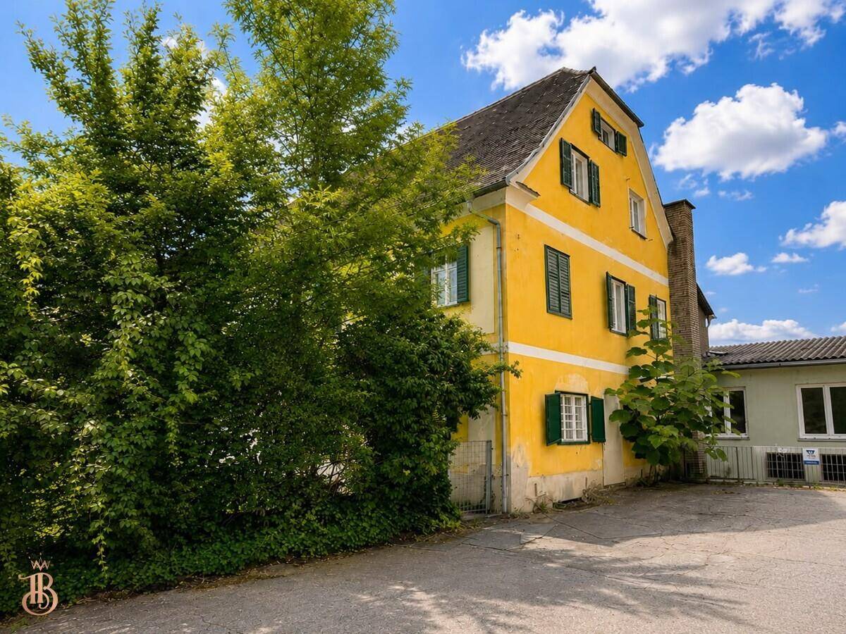 Seitenansicht des gelben Gebäudes mit üppiger Begrünung und angrenzendem Nebengebäude.