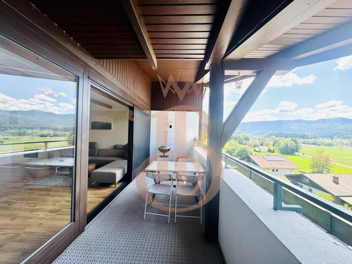 Überdachter Balkon mit Esstisch und Stühlen, bietet einen weiten Blick auf die grüne Landschaft.