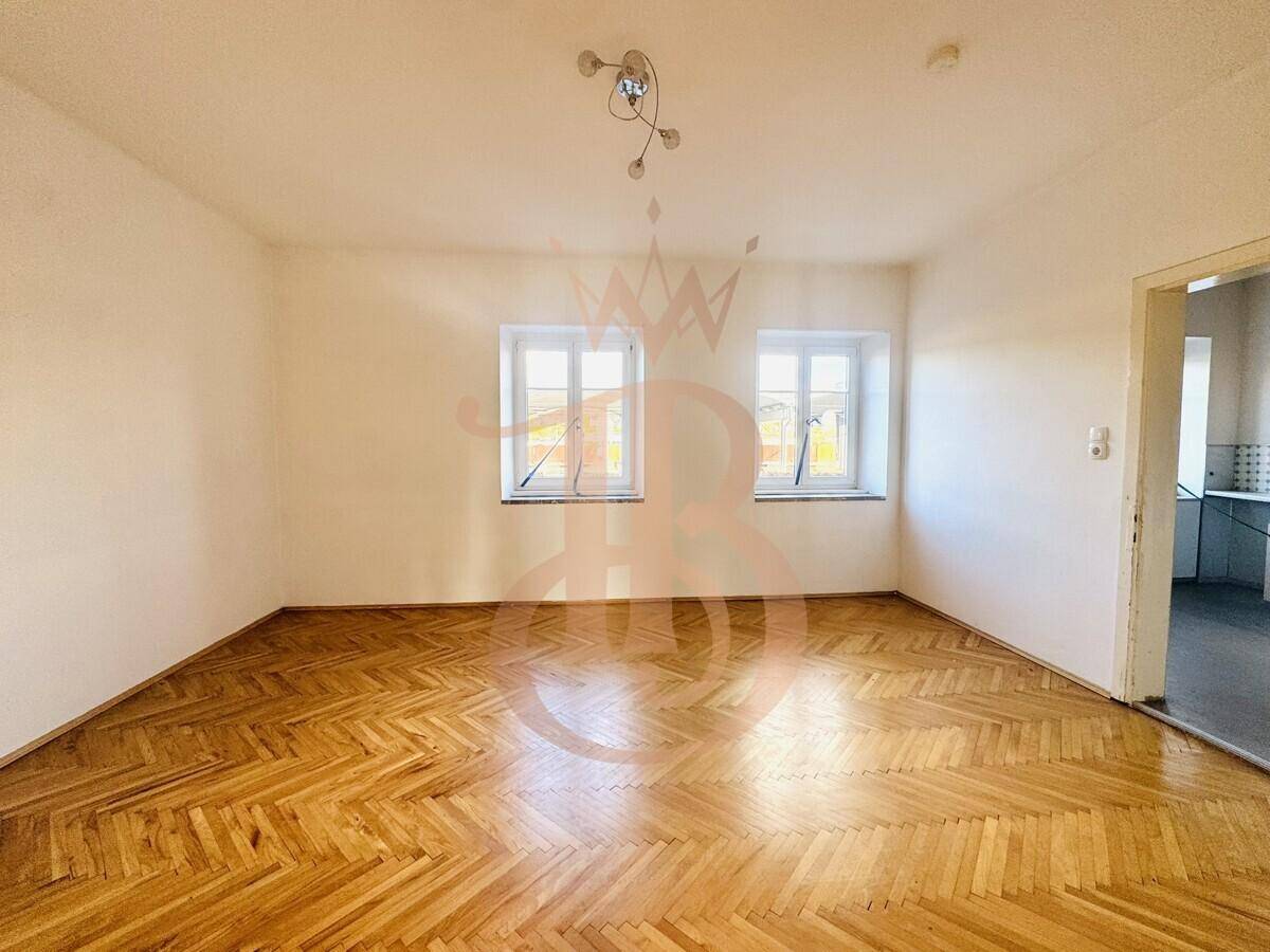 Geräumiges Zimmer mit Fischgrätparkettboden und zwei Fenstern, das hell und einladend wirkt.