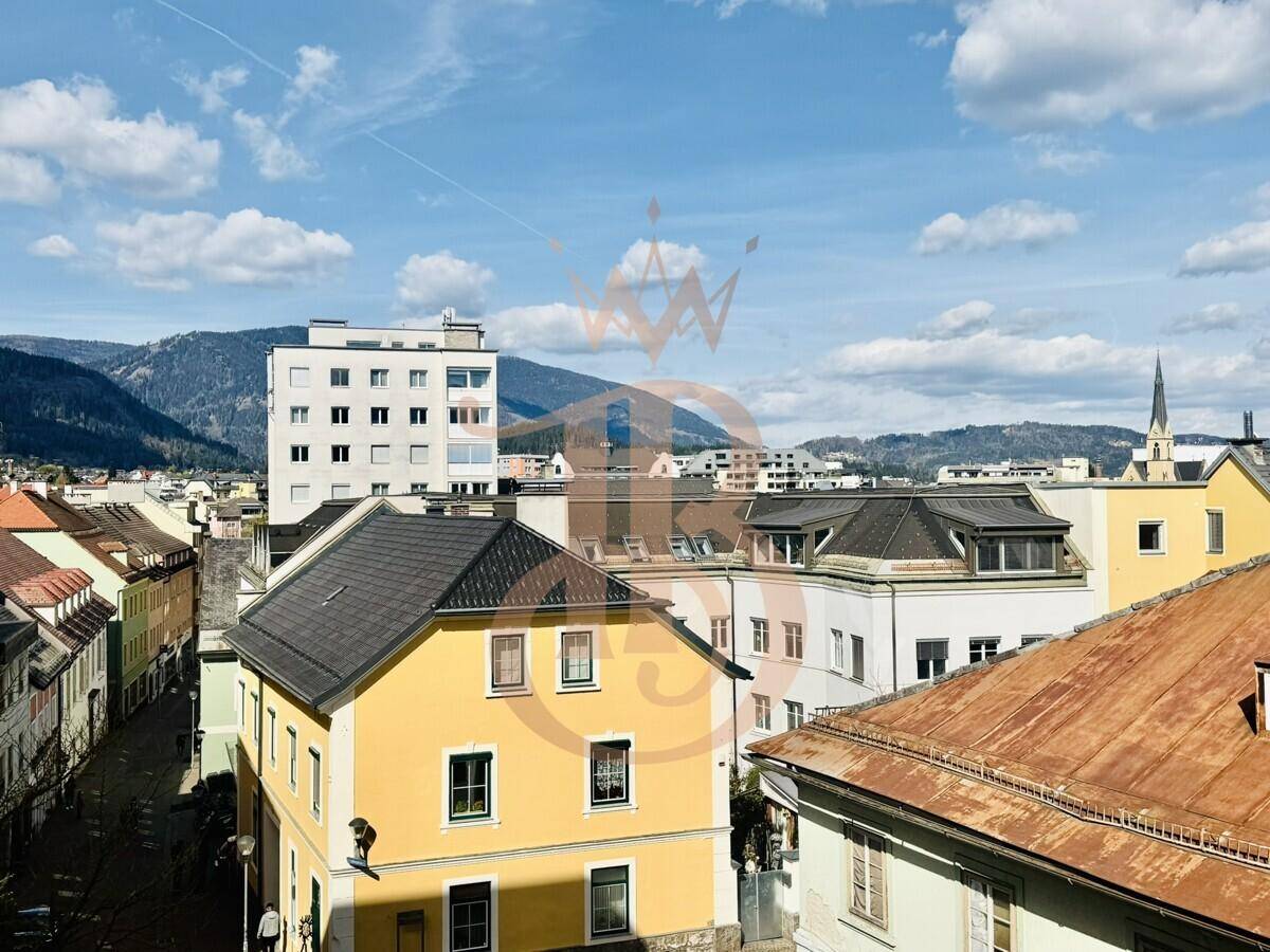 Panoramablick über die Stadt mit verschiedenen Gebäuden und Bergen unter einem bewölkten Himmel.