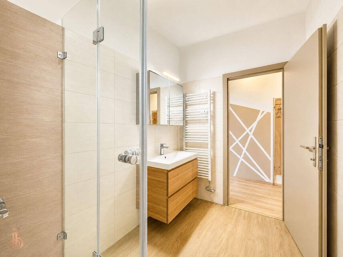 Helles Badezimmer mit Duschkabine, Holzwaschtisch, beheiztem Handtuchhalter und Spiegelschrank.