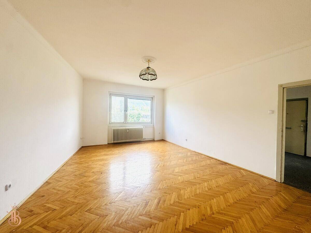 Helles Zimmer mit Fischgrätparkett, weißer Decke und Fenster mit Blick ins Grüne.