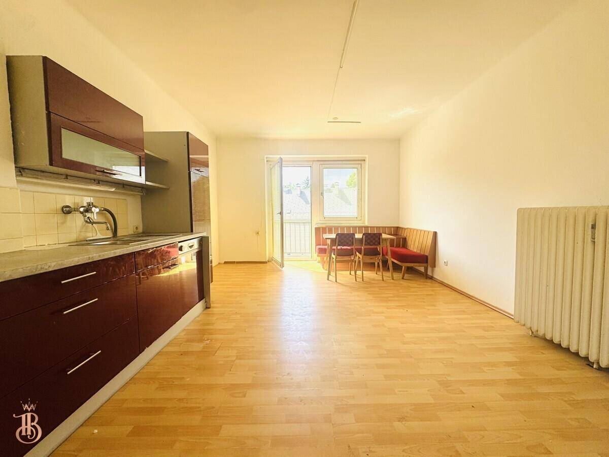 Offener Wohn-Essbereich mit Küchenzeile, Laminatboden und direktem Zugang zum Balkon.