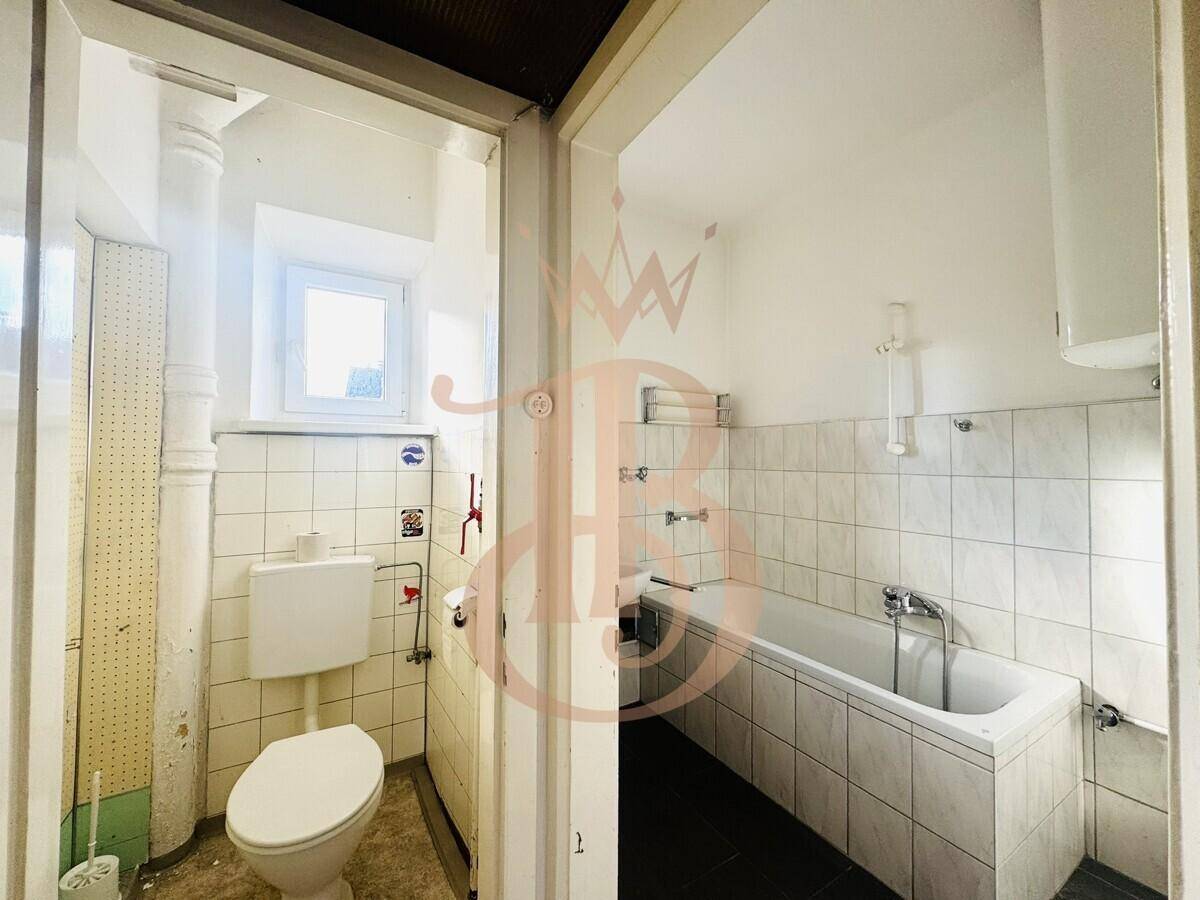 Badezimmer mit Badewanne, Toilette und Fenster, das für Belüftung und Tageslicht sorgt.