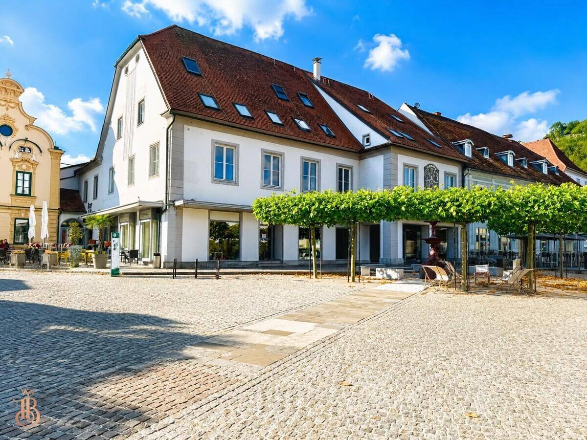 Historisches Gebäude mit rotem Ziegeldach und Dachfenstern an einem sonnigen Stadtplatz.
