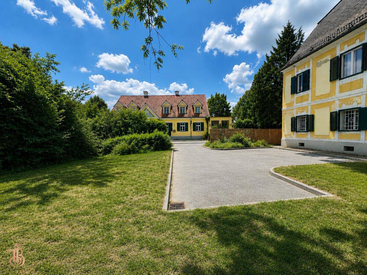 Weitläufiger Außenbereich mit gepflegtem Rasen, Parkplatz und weiteren Gebäuden im Hintergrund.