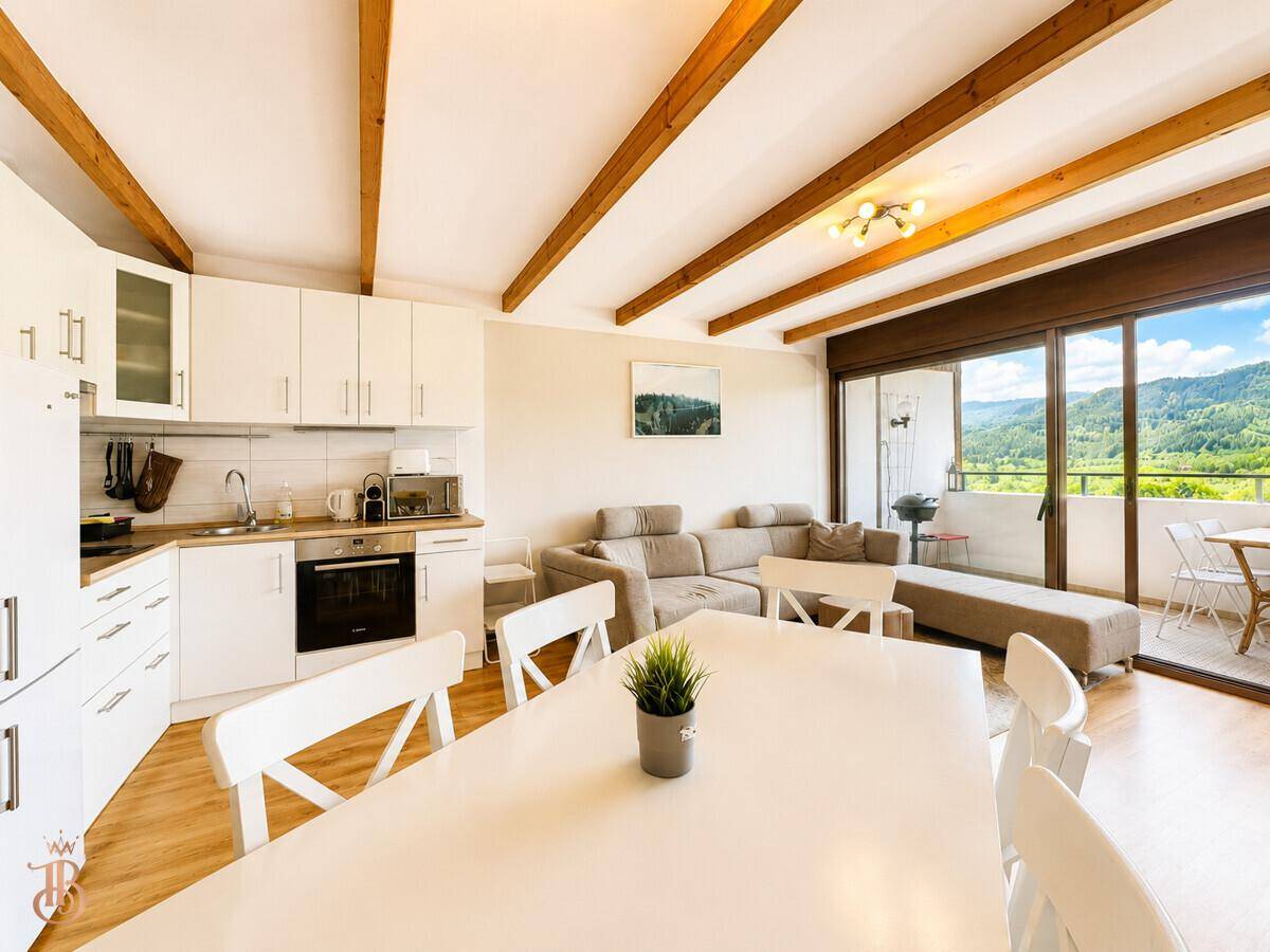 Offener Wohn-Essbereich mit moderner weißer Küche und direktem Zugang zum sonnigen Balkon.