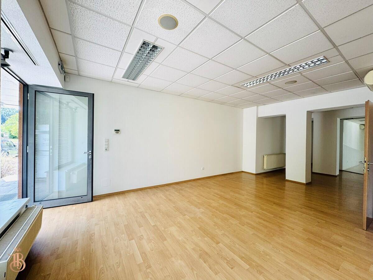 Geräumiger Büroraum mit Holzfußboden, abgehängter Decke und Zugang nach draußen.